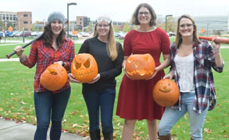 Miranda Nehrig, Hannah Johnson, Elizabeth Hyde, and Morgan Daly holding pumpkins in the courtyard