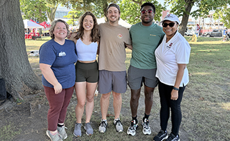 five people standing together under a tree in a park