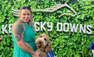woman posting with her service dog in front of a sign for Kentucky Downs
