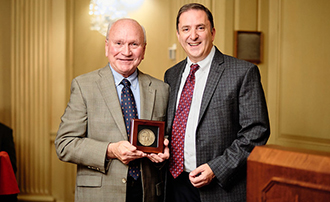two men standing next to each other in a ballroom, one of whom has just received an award