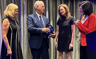 three women talking with a man who has received an award