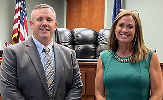 A man and a woman wearing business professional attire standing in front of a judge's bench